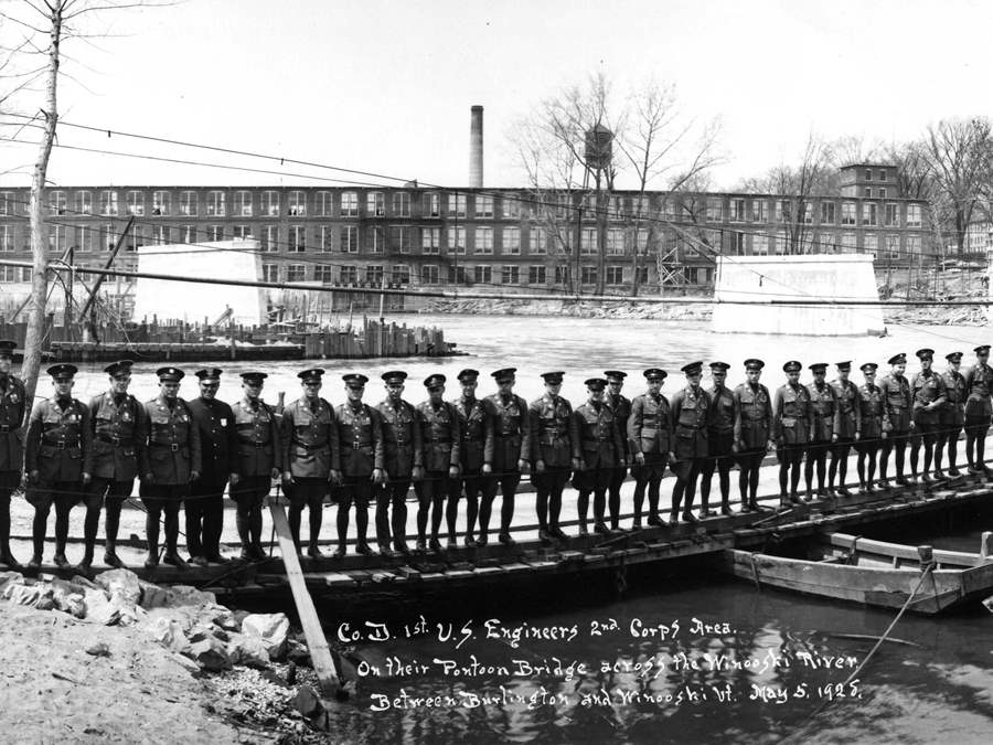 Military men lined up along the Winooski River wearing uniforms manufactured in the Champlain Mill
