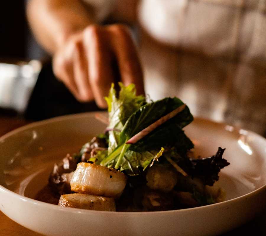 Waterworks' scallops entrée is seen, about to be enjoyed by a guest who has already extended their fork towards the dish.